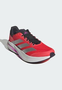 Red running shoe with black laces, grey stripes on the side, and a white and purple sole. Lightweight mesh upper for breathability.