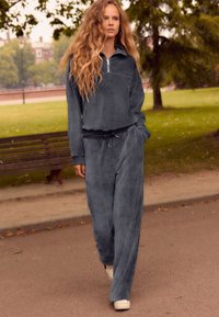 Survêtement en velours côtelé gris avec col zippé, manches longues et pantalon ample avec taille élastique et poches latérales.