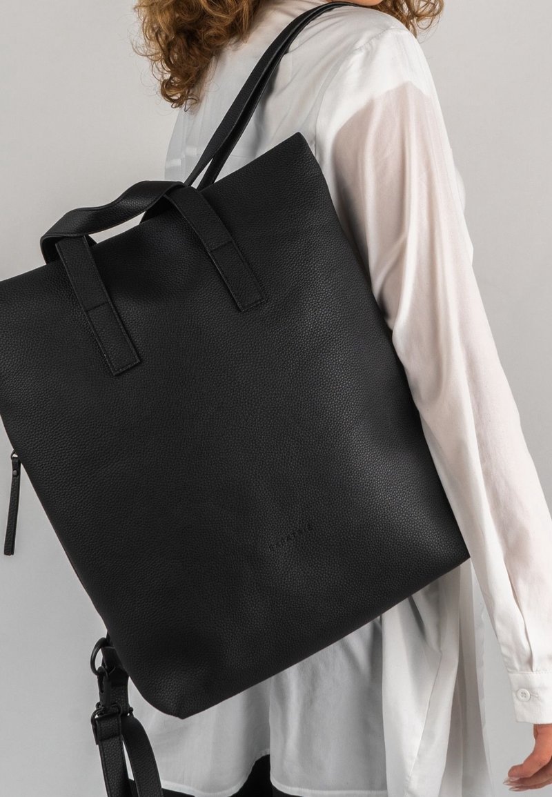 Czarny skórzany plecak o fakturowanej powierzchni, z dwoma górnymi uchwytami i odpinanym paskiem. Minimalistyczny design, bez widocznych logo i wzorów.
