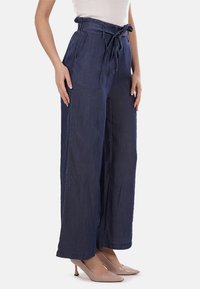 Pantaloni in denim blu navy a gamba larga, con vita alta, cintura da annodare e tasche laterali, caratterizzati da una superficie liscia e da una vestibilità rilassata.