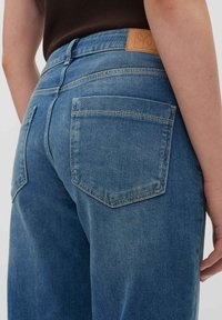 Blauwe denim jeans met een hoge taille, voorzien van twee achterzakken, versterkte stiksels en een tan leren label bij de taille.