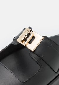 Sandale en cuir noir avec une large sangle présentant une grande boucle dorée brillante avec le logo Furla.