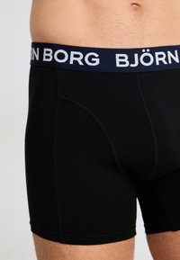 Nærbilde av en person som har på seg svarte Björn Borg boxertruser med en marineblå midjebånd og hvit logo.