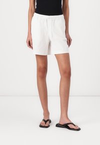 Pantaloni corti bianchi in cotone con vita elastica e stringa, caratterizzati da una vestibilità comoda e orlo dritto. Abbinati a infradito nere.