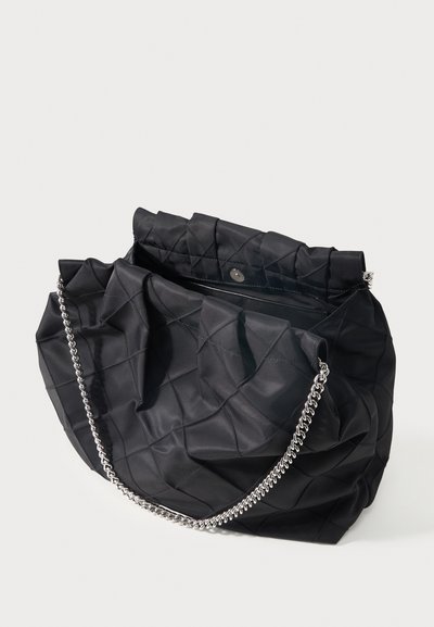 Μαύρη καπιτονέ τσάντα χειρός με ασημένιο αλυσίδα, ανοιχτό πάνω μέρος με μαγνητικό κλείσιμο, εμφανίζεται σε λευκό φόντο.