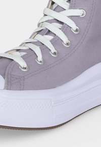 Κοντινή λήψη ενός ανοιχτό μοβ καμβά sneaker με λευκά κορδόνια και παχύ λευκό λαστιχένιο πέλμα.