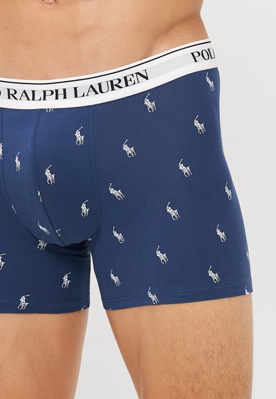 Mornarsko modri bokserice iz bombaža, okrašene z belimi logotipi polo igralcev v ponavljajočem se vzorcu, z blagovno znamko v črno-beli barvi na pasu.