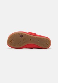Zapato superior suave rojo con suela de goma marrón flexible, que presenta un diseño texturizado y una correa de velcro para un ajuste seguro.