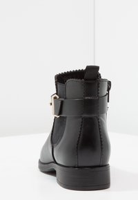 Botín de cuero negro con paneles elásticos en los laterales, detalles con forma de ondas y un accesorio de hebilla en tono dorado. Tacón bajo y resistente con acabado texturizado.