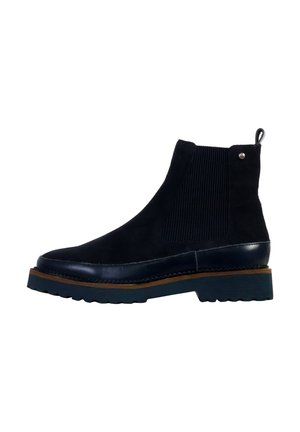 Botte Chelsea en daim noir avec panneau latéral élastique, bordure brune sur la semelle et semelle extérieure en caoutchouc noir rainurée.