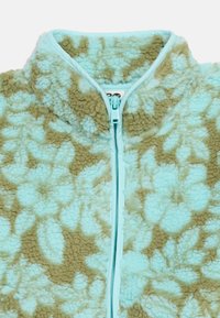 Niebiesko-brązowa kurtka z polaru w kwiatowy wzór z przednim zamkiem błyskawicznym częściowo zapiętym, na białym tle.