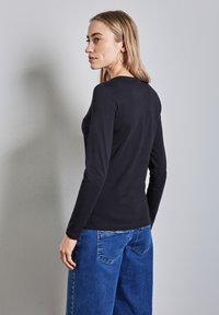 Musta pitkähihainen paita, joka on valmistettu pehmeästä kankaasta, pyöreäkauluksinen ja slim fit -mallinen, yhdistetty löysiin sinisiin farkkuihin.