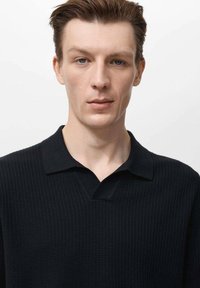 Polo shirt nera lavorata a maglia con scollatura a V e maniche corte, caratterizzata da un motivo testurizzato e un design del colletto liscio.