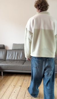 Heleroheline ja valge fliispusa, millel on kõrge krae ja tekstuuriga kangas, kombineeritud laiade siniste teksadega. Näha on puidust põrand.