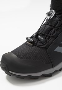 Czarne buty trekkingowe z teksturowaną cholewką, wyposażone w system sznurowania typu bungee, wzmocniony czubek oraz logo Gore-Tex zapewniające wodoodporność.