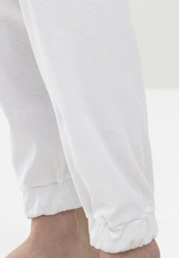 Witte joggingsbroek gemaakt van zachte stof, met elastische boorden met een glanzende afwerking bij de enkels. De textuur oogt glad en ontspannen.
