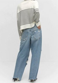 Kremowy dzianinowy sweter w czarne paski, zestawiony z jasnoniebieskimi, szerokimi spodniami z postrzępionymi detalami. Teksturowana tkanina i wykończenie z postrzępionym brzegiem.