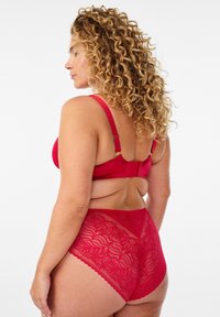 Czerwony koronkowy biustonosz i pasujące wysokie majtki z misternymi wzorami liści. Regulowane ramiączka i zapięcie na haftki w biustonoszu.