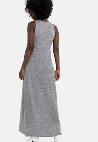 Długa, szara sukienka dzianinowa bez rękawów o luźnym kroju, z okrągłym dekoltem i prążkowaną fakturą, sięgająca tuż ponad kostkę.
