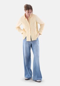 Yellow long-sleeve button-up shirt with a soft texture, paired with light blue wide-leg denim jeans displaying a classic wash and loose fit.