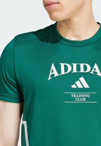 Grønn treningstrøye laget av glatt stoff. Har hvit "ADIDAS" logo og "TRAINING CLUB" tekst. Rund hals og korte ermer.