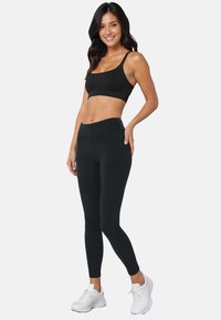 Set van een zwarte sportbeha en legging gemaakt van rekbaar materiaal, met een aansluitend ontwerp en hoge taille ondersteuning, gecombineerd met witte sportschoenen.