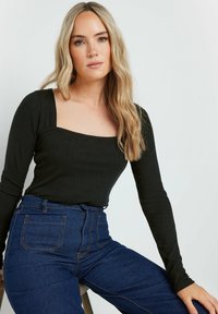 Schwarzes, geripptes Langarmoberteil mit quadratischem Ausschnitt, kombiniert mit hochgeschnittenen dunkelblauen Jeans aus Denim mit Gesäßtaschen und kontrastierenden Nähten.