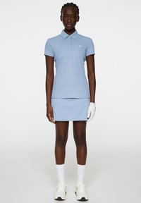 Jasnoniebieski zestaw polo i spódnicy, wykonany z teksturowanej tkaniny. Posiada kołnierzyk, krótkie rękawy oraz logo na piersi.