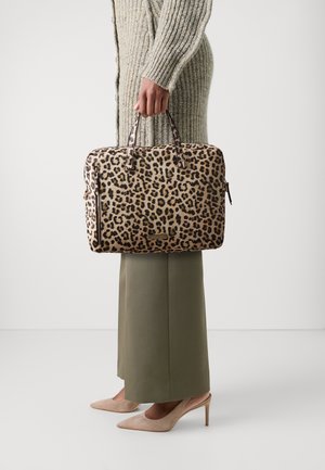 Sac d'ordinateur portable à imprimé léopard avec poignées en cuir marron, forme rectangulaire et tissu texturé. Porté avec un pantalon vert olive et des talons beiges.