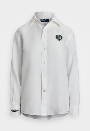 Camisa de linho branca com um design verde de coração bordado, ornamentado com folhas de louro no peito, três botões e detalhe de punho com marca.