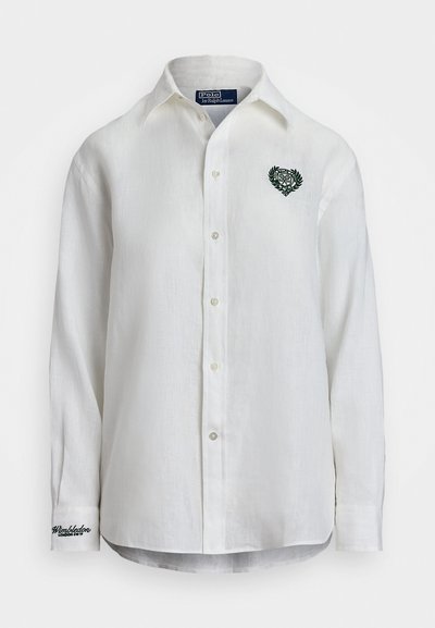 White linen shirt featuring a green embroidered heart design with laurel leaves on the chest, three buttons, and branded cuff detail.