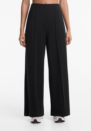 Schwarzweisse Wickelhosen mit hoher Taille, ausgestattet mit vorderen Falten und einer glatten Textur. Kombiniert mit hellen Sneakers.
