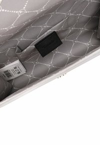 Světlé šedé vnítřní části tašky s geometrickým vzorem. Obsahuje černou nášivku s logem, štítek a hladkou saténovou texturu.
