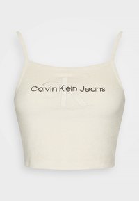 Krátký krémový top z měkké látky. Na přední straně tmavé vyšívání s logem Calvin Klein Jeans, tenké nastavitelné ramínka.