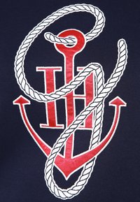 Tessuto blu navy con motivo di un'ancora rossa intrecciata con una corda bianca e lettere rosse "HH" al centro.