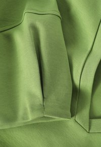 Gros plan sur un tissu vert clair avec des coutures visibles et des couches pliées montrant les détails de la texture et de la couture.