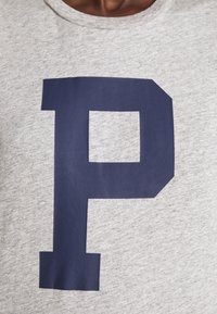 Grå bomulls-t-shirt med ett stort marinblått bokstav "P" med ett fyrkantigt urtag i designen. Korta ärmar och rundad halsringning.