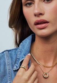 Guldpläterade halsband med en cirkulär berlock, en texturerad ring och en krage av denimjacka. Släta texturer och blanka metalldetaljer.