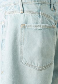 Světle modré džíny šortky mají roztrhnutou zadní kapsu s kontrastním šitím. Tkanina má jemnou strukturu a vybledlý design.