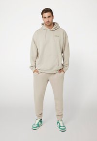 Bežinė sudedamoji su priekinėmis kišenėmis ir raišteliais, derinama su atitinkančiais džinsais. Yra mentes teal ir baltos spalvos sportbačiai. Paprastas, minimalistiškas dizainas.