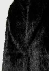 Crni kaput od umjetnog krzna s mekom, gustu teksturom i dizajnom sa šalom. Materijal ima sjajnu završnicu s vlaknima različitih duljina.