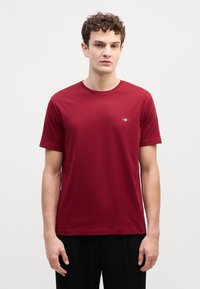 Burgundy lyhythihainen T-paita puuvillasta, pyöreä kaula-aukko, pieni logo vasemmassa rinnassa. Sileä pinta ja rento istuvuus.