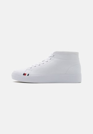 Baskets montantes blanches avec lacets et un petit détail de rayure rouge, blanche et bleue près de la semelle sur un fond uni.