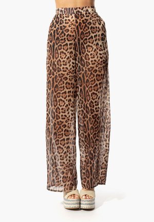 Pantalones anchos de diseño de leopardo, translúcidos, con cintura alta y textura suave. La tela presenta patrones en marrón y negro. Combinados con sandalias de plataforma.