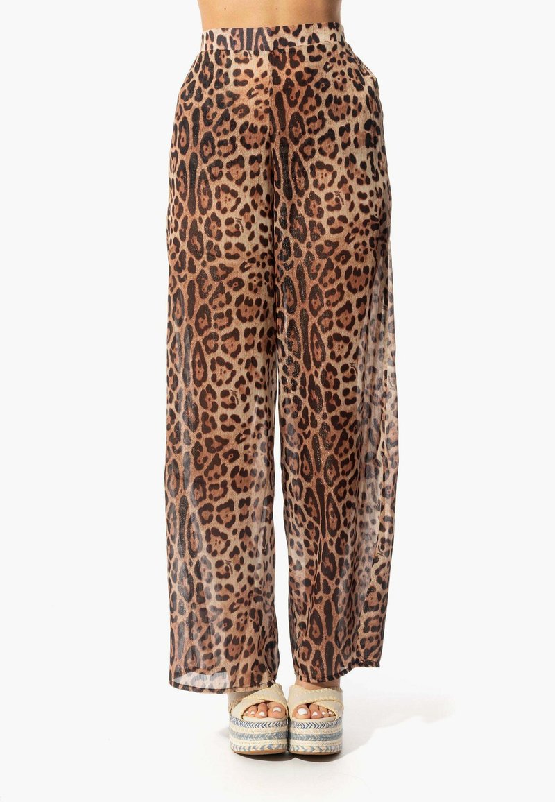 Pantaloni larghi a fantasia leopardata trasparenti con vita alta e texture liscia. Il tessuto presenta motivi marroni e neri. Indossati con sandali con zeppa.