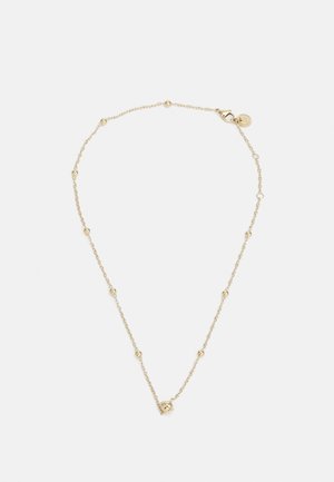 Collier délicat en chaîne d'or avec de petites perles espacées uniformément et un fermoir mousqueton avec une étiquette ronde sur fond blanc.