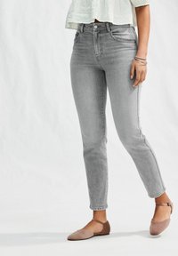 Vaqueros de mezclilla gris con un ajuste slim, diseño de cinco bolsillos y cierre de botón. Combinados con unos zapatos planos marrón claro y un top corto.