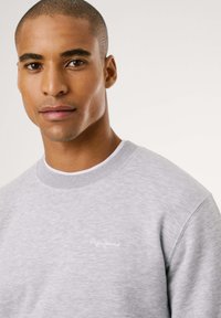 Sudadera gris con cuello de punto, que presenta un pequeño logo blanco de "Pepe Jeans" en el pecho. Textura suave y diseño casual.