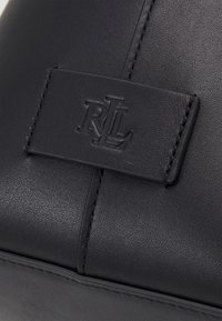 Svart läderväska med en texturerad yta, sömnadsdetaljer och en slät läderaccent med ett präglat logotyp.