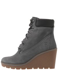 Stivaletti alla caviglia in suede grigio con tacco a zeppa, design con lacci, suola in gomma texturizzata e collo imbottito nero. Logo Timberland sul lato.